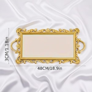 Pode incluir: Uma bandeja retangular dourada com uma moldura ornamentada de volutas e duas al&ccedil;as laterais. A bandeja apresenta uma superf&iacute;cie central lisa e plana. As dimens&otilde;es est&atilde;o claramente marcadas como 48 cm de comprimento e 3 cm de altura.