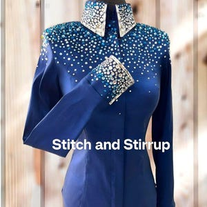 Könnte beinhalten: Ein marineblaues Langarmhemd mit Kragen und Manschetten, verziert mit glitzernden Strasssteinen. Das Hemd zeigt den Text "Stitch and Stirrup" in Weiß. Das Design ist wahrscheinlich für Reitveranstaltungen.