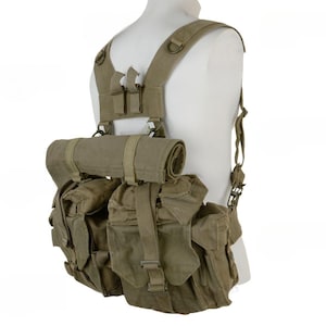 May include: An olive drab canvas tactical harness system featuring a series of modular pouches and a rolled fabric component attached to the upper section. The gear includes adjustable shoulder straps, metal D-rings, and secure buckle closures.
