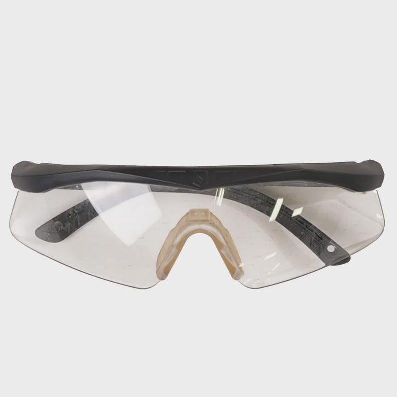 Pu&ograve; includere: Occhiali di sicurezza trasparenti con montatura nera e nasello beige. Le lenti sono chiare e angolate, offrendo un ampio campo visivo. Design sportivo e moderno, adatti a varie attivit&agrave;.