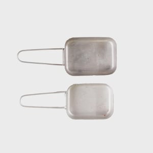 May include: Two rectangular, silver-colored metal mess kits with attached wire handles. The kits have rounded corners and a slightly worn appearance, suggesting they are vintage or used. The handles are in a U-shape.