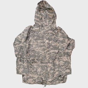May include: A camouflage jacket with a hood, featuring a digital pattern in shades of grey, beige, and green. The jacket has a drawstring hem and two front pockets. The hood is attached and the sleeves have adjustable cuffs.