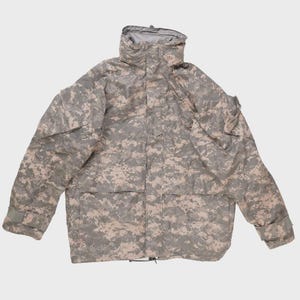 May include: A camouflage pattern jacket with a hood. The jacket features a digital camouflage design in shades of gray, tan, and green. It has multiple pockets, a drawstring at the waist, and a full-length zipper. The jacket is designed for outdoor wear.