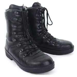 May include: A pair of black leather high-top boots featuring a textured finish, rounded toes, and thick black rubber soles. The boots have black laces threaded through metal eyelets and hooks, extending up the shaft to provide ankle support.
