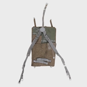 May include: A vintage military backpack in shades of green and brown, featuring a unique raindrop camouflage pattern. The pack has adjustable gray straps and multiple compartments, with metal buckles and fasteners.