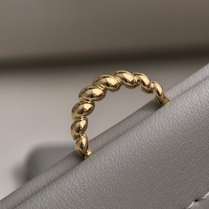 Puede incluir: Un anillo de oro con un diseño ovalado repetido. El anillo está hecho de oro pulido y tiene una superficie lisa y reflectante. El anillo es una joya sencilla pero elegante.