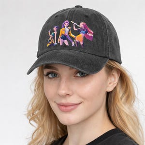 Puede incluir: Gorra de béisbol gris oscuro con un gráfico colorido de tres figuras estilizadas. Las figuras están representadas en colores vibrantes, una de ellas con una chaqueta amarilla. La gorra tiene una visera curva y un diseño clásico de seis paneles.