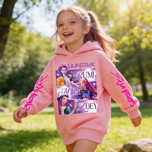 May include: A light pink hooded sweatshirt featuring the text "HUNTRAX" and the names "RUMI", "MIRA", and "ZOEY" in a purple and white design. The sleeves have the text "Skin Boys" and "Crossfire" in a pink script. The sweatshirt is worn by a young person.