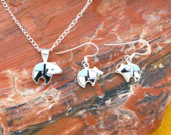 May include: A silver jewelry set consisting of a pendant on a chain and two matching drop earrings. Each piece features a bear-shaped inlay made of segmented black, white, and light blue stone pieces set within a polished silver frame.