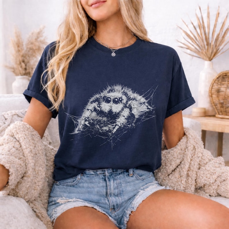 Pu&ograve; includere: T-shirt blu navy scuro con un'illustrazione dettagliata in scala di grigi di un ragno saltatore. Il ragno &egrave; il punto focale, con dettagli intricati del suo corpo e dei suoi occhi. La maglietta &egrave; in stile casual, adatta all'uso quotidiano.