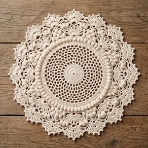 May include: Cream-colored, circular crochet doily with intricate openwork and a scalloped edge. The handmade doily features a central spiral design surrounded by concentric rings of textured stitches and decorative elements. The doily is displayed on a wooden surface.