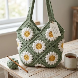 May include: A handmade green crochet tote bag with white and yellow daisy flower appliqués. The bag has a tag that reads "THE RETRO DAISY TOTE - Handmade with love." A ball of green yarn and a crochet hook are next to the bag.