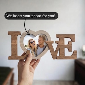 Peut inclure: Cadre photo en bois avec le mot "LOVE", un cœur pour une photo. La main tient le cadre avec une photo d'un couple. Le texte "We insert your photo for you!" est au-dessus du cadre.