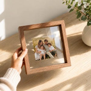 Peut inclure: Un cadre flottant carré en bois avec une finition à grain brun naturel, doté d'une vitre transparente contenant une photographie d'une famille de quatre personnes assises dans un champ d'herbe, montrant une mère, un père, une fille et un garçon.