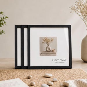 Peut inclure: Un ensemble de trois cadres photo carrés noirs avec passe-partout blanc. L'avant du cadre affiche le texte PHOTO FRAME 20x20cm/8x8inch. Chaque cadre présente un design simple et épuré avec une fine bordure noire et une vitre de protection.