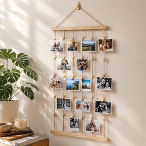 Può includere: Un espositore da parete per foto composto da due barre orizzontali in legno chiaro collegate da cinque corde di iuta verticali. Piccole mollette in legno sono fissate alle corde per sostenere quattordici fotografie rettangolari.