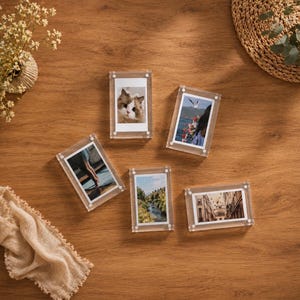 Peut inclure: Cinq cadres photo magnétiques en acrylique transparent disposés sur une surface. Chaque cadre contient une photographie différente : un chat, une scène côtière avec un oiseau, des jambes, un paysage forestier et une vue de rue urbaine.