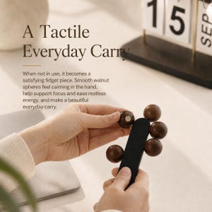 May include: A fidget toy featuring a black rectangular base with five dark brown wooden spheres attached by magnets. The text on the image reads: A Tactile Everyday Carry. When not in use, it becomes a satisfying fidget piece. Smooth walnut spheres feel calming in the hand, help support focus and ease restless energy, and make a beautiful everyday carry.