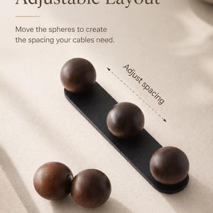May include: A cable management system featuring a black rectangular base and dark brown wooden spheres. The text reads: Magnetic Holders, Adjustable Layout. Move the spheres to create the spacing your cables need. Adjust spacing.