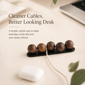 May include: A cable organizer featuring five dark brown wooden spheres mounted on a slim, horizontal black base. The text Cleaner Cables, Better Looking Desk and A simple, stylish way to keep everyday cords tidy and your setup refined is visible.