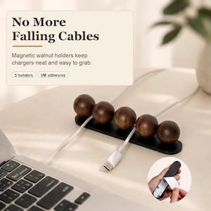 May include: A magnetic cable organizer featuring five dark walnut wooden spheres mounted on a black rectangular base. The text on the image reads No More Falling Cables, Magnetic walnut holders keep chargers neat and easy to grab, 5 holders, 3M adhesive.