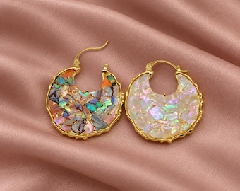 May include: A pair of gold-toned hoop earrings featuring a crescent-shaped design. One earring is inlaid with iridescent, multi-colored abalone shell fragments, while the other earring is inlaid with shimmering, pearlescent white shell pieces.