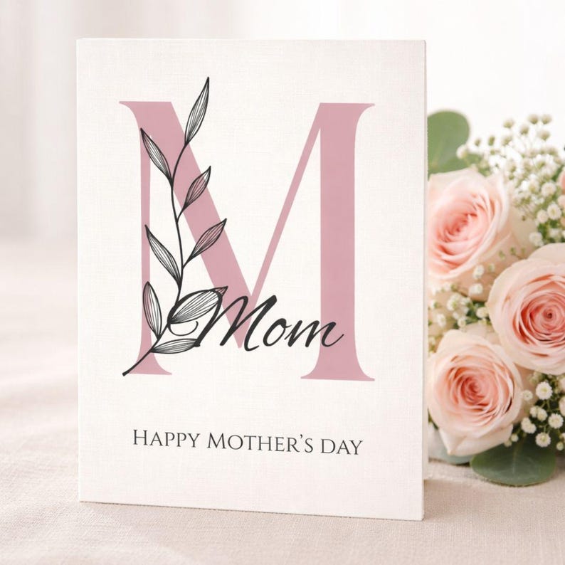 Może przedstawiać: Biała kartka na Dzień Matki z dużą r&oacute;żową literą "M" i słowem "Mom" w skrypcie. Czarny kwiatowy wz&oacute;r zdobi literę. Tekst "HAPPY MOTHER'S DAY" znajduje się na dole. R&oacute;żowe r&oacute;że w tle.