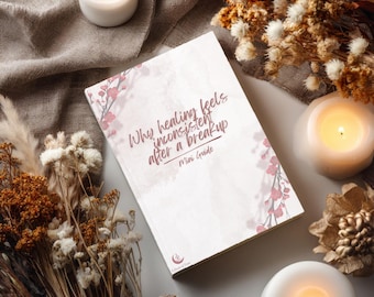 Pode incluir: Um livro retangular com capa branca apresentando ramos de cerejeira em flor cor-de-rosa e o texto Why healing feels inconsistent after a breakup Mini Guide. O livro está rodeado por flores secas e três velas brancas acesas.