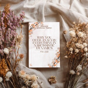 May include: A book titled Why You Over-Analyze Everything in Narcissistic Dynamics Mini Guide with a white cover featuring brown text and delicate orange floral illustrations on the top left and bottom right corners, centred on a neutral fabric.