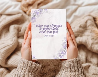 Pode incluir: Um livreto retangular com capa branca apresentando detalhes florais roxos nos cantos e o texto Why you struggle to understand what you feel Mini Guide impresso em letra cursiva roxa. Um pequeno logotipo de lua e estrela roxo está na parte inferior.