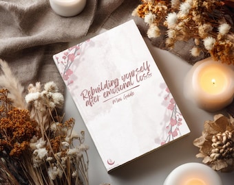 Pode incluir: Um livro branco intitulado Rebuilding yourself after emotional loss Mini Guide com ilustrações de ramos floridos cor-de-rosa na capa. O livro apresenta um pequeno logótipo de meia-lua na parte inferior e está rodeado por flores secas e velas.