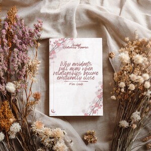 Puede incluir: Un libro rectangular titulado Avoidant Relationship Dynamics: Why avoidants pull away when relationships become emotionally close, Mini Guide. La portada presenta un fondo blanco con detalles florales rosas y un pequeño logotipo de media luna.
