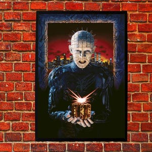 May include: A framed poster featuring a character from the horror film Hellraiser. The character, with a pale face and pins in their head, holds a glowing puzzle box. The background shows a cityscape under a red sky.