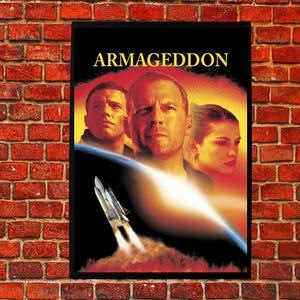 Könnte beinhalten: Ein gerahmtes Filmplakat für "Armageddon" mit Bruce Willis und anderen. Das Poster hat einen schwarzen Rahmen und ist vor einer roten Backsteinmauer angebracht. Der Titel ist in goldenen Buchstaben, und das Bild zeigt ein startendes Raumschiff.