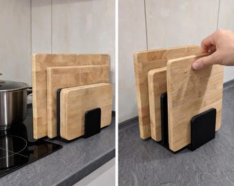 May include: Wooden chopping boards of different sizes in a black metal holder. The boards are made of light-coloured wood and are stacked vertically. A stainless steel saucepan sits on a black hob.