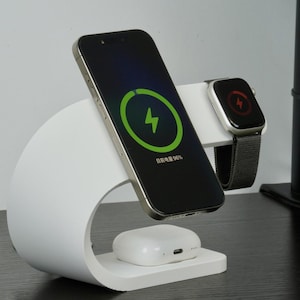 Può includere: Stazione di ricarica bianca dal design curvo, che tiene uno smartphone nero, uno smartwatch e una custodia di ricarica wireless bianca. Lo schermo del telefono mostra un simbolo di ricarica verde. Lo smartwatch mostra un simbolo di ricarica rosso.