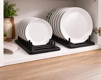 May include: Two black plate racks holding stacks of white plates inside a white cupboard. The plates are round and have a simple design. The racks are made of a dark material and have vertical dividers to hold the plates upright.