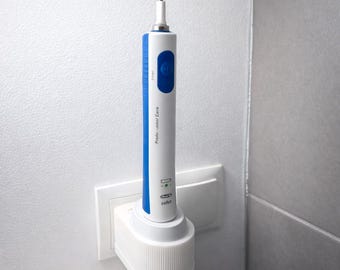 May include: An electric toothbrush in a white and blue design, docked in its charging base, which is plugged into a wall socket. The toothbrush is labelled "Professional Care". The base is white with a ribbed pattern.