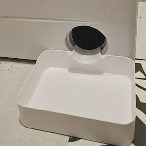 Può includere: Un distributore d'acqua per animali domestici in plastica bianca con una vaschetta rettangolare e un'apertura circolare sul retro. L'unità presenta un design liscio con un beccuccio curvo che dirige l'acqua nella vaschetta bassa.