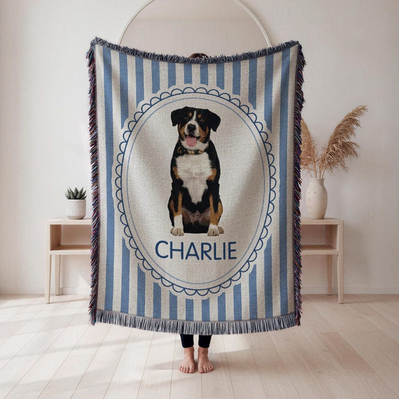 May include: A woven throw blanket with a blue and white striped pattern and a decorative border. The center features a portrait of a dog with the name "CHARLIE" below. The blanket has fringed edges.