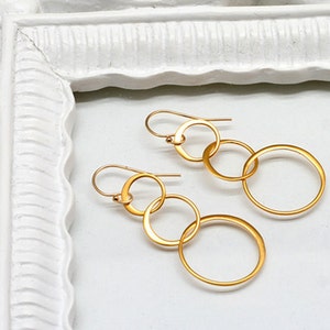 May include: Gold-toned earrings with multiple interlocking circles. The earrings are dangling and have a simple hook closure.