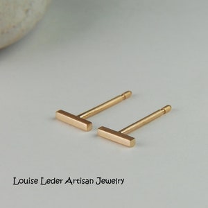 May include: A pair of gold bar stud earrings. The earrings are simple and minimalist, with a straight bar design.
