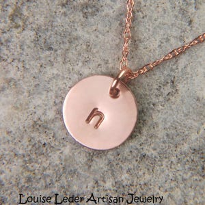 May include: A rose gold necklace featuring a small, circular pendant stamped with the lowercase letter h. The pendant hangs from a delicate, twisted chain. The text Louise Leder Artisan Jewelry is printed at the bottom of the image.