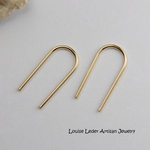 May include: A pair of gold-toned minimalist earrings with a simple arch shape. The earrings are made of a thin, smooth metal and have a polished finish.