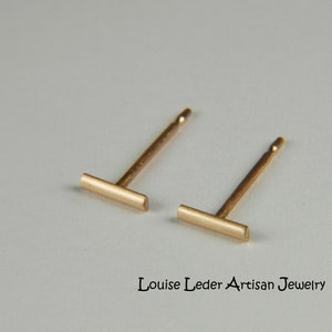 Puede incluir: Un par de pendientes de barra de oro. Los pendientes son simples y minimalistas, con una peque&ntilde;a barra rectangular.