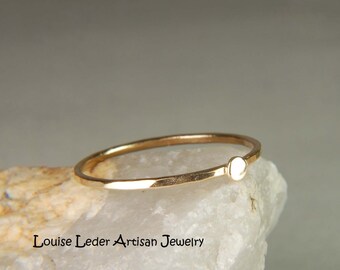 May include: A simple gold ring with a small, round, white accent. The ring is on a white rock.
