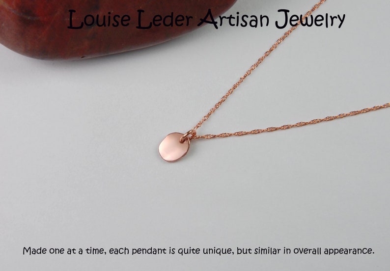 Puede incluir: Un collar de oro rosa con un peque&ntilde;o colgante redondo. La fina cadena se muestra sobre un fondo blanco. El texto "Louise Leder Artisan Jewelry" es visible en la parte superior. El texto en la parte inferior dice: "Hecho uno a la vez..."