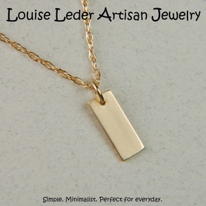 May include: A gold-colored rectangular pendant necklace. The pendant hangs from a delicate gold chain. The jewelry is displayed against a neutral background. The text "Louise Leder Artisan Jewelry" is at the top.