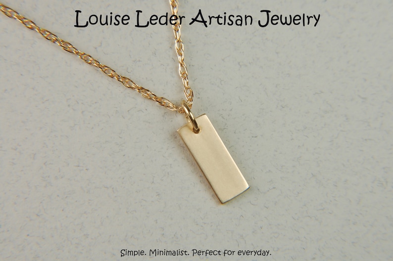 May include: A gold-colored rectangular pendant necklace. The pendant hangs from a delicate gold chain. The jewelry is displayed against a neutral background. The text "Louise Leder Artisan Jewelry" is at the top.