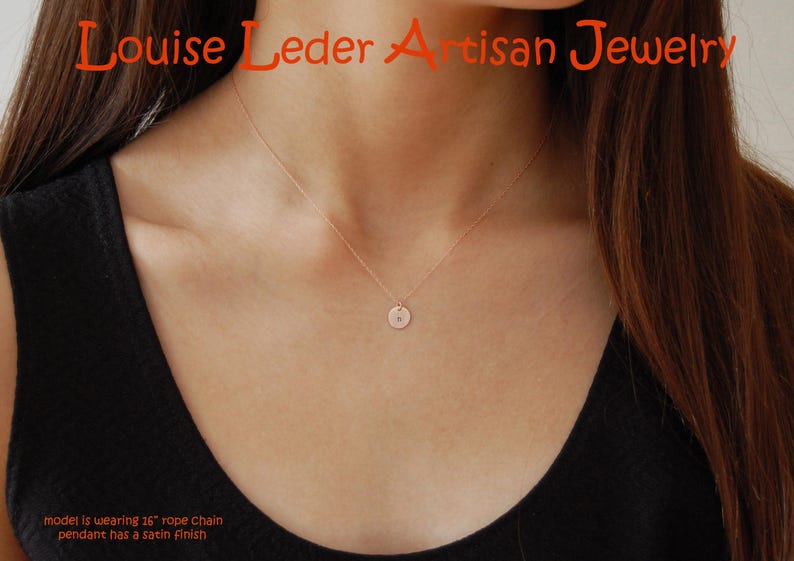May include: A rose gold necklace featuring a small circular pendant with a satin finish on a 26-inch rope chain. The text Louise Leder Artisan Jewelry is visible at the top, and the text model is wearing 26-inch rope chain pendant has a satin finish is at the bottom.